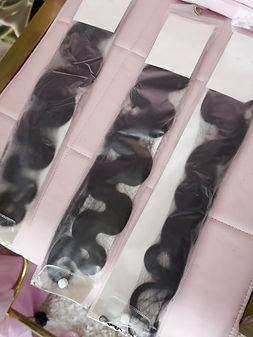 Long, black, wavy hair extensions in plastic packaging on a pink surface.